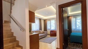 A hotel room with a wooden staircase, a sofa, a chair, and a bed with a blue cover. - Flora Uzungol Resort Hotel (Çaykara)