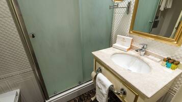 A bathroom with a glass shower enclosure, a sink with a marble countertop, and a mirror with a gold frame.