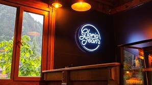 A restaurant interior with a neon sign reading "Gloria Jeans," wooden ceiling, and a window overlooking greenery. - Flora Uzungol Resort Hotel (Çaykara)