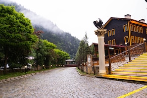 A cobblestone street leading to a building with a reception sign, surrounded by lush greenery and mountains in the background. - Flora Uzungol Resort Hotel (Çaykara)