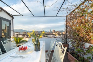 A terrace with a table set for two, a potted plant, and a view of a cityscape. - Pitti Luxury Terrace by Mmega (Florence)