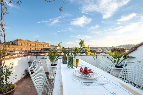 A terrace with a table set for two, featuring a plate of strawberries, a glass of white wine, and a vase with yellow flowers. - Pitti Luxury Terrace by Mmega (Florence)