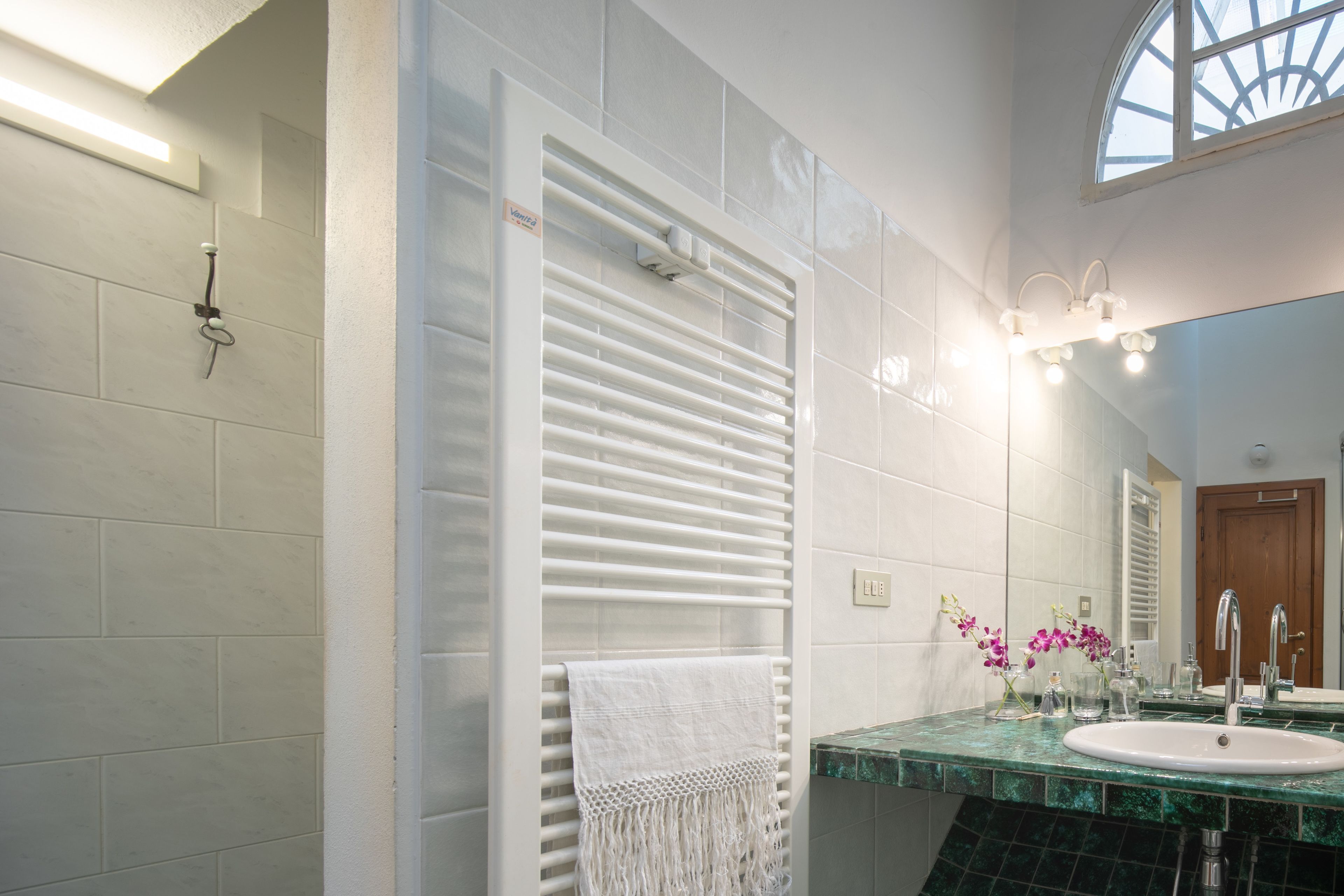 A modern bathroom with a white towel rack, a green marble sink, and a large mirror.