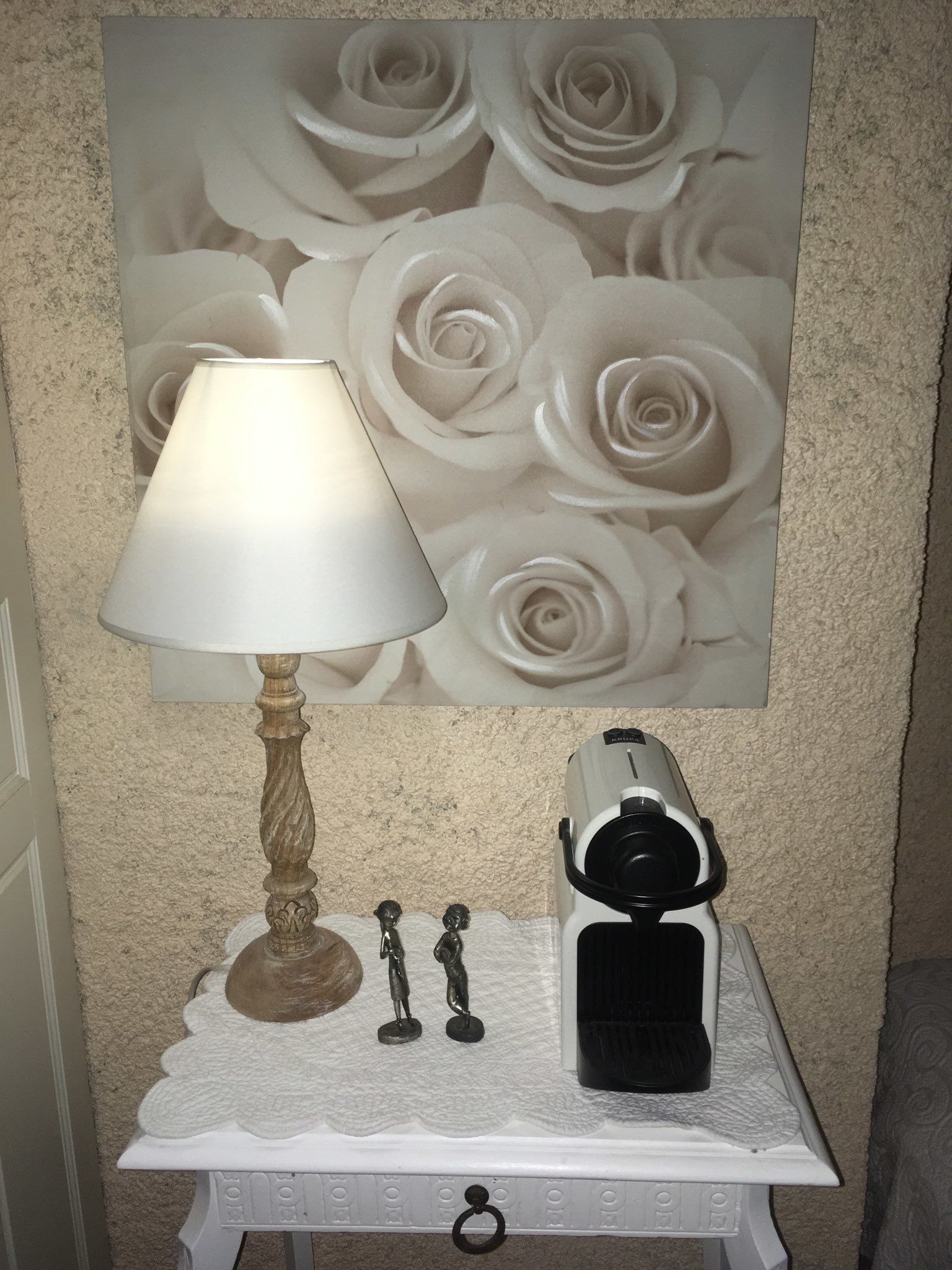Ein kleiner Tisch mit einer Lampe, einer Kaffeemaschine und einem dekorativen Gegenstand vor einer strukturierten Wand.
