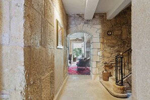 A stone-walled hallway with a red carpet, a chair, and a basket near a staircase. - L'Orangerie (Valros)
