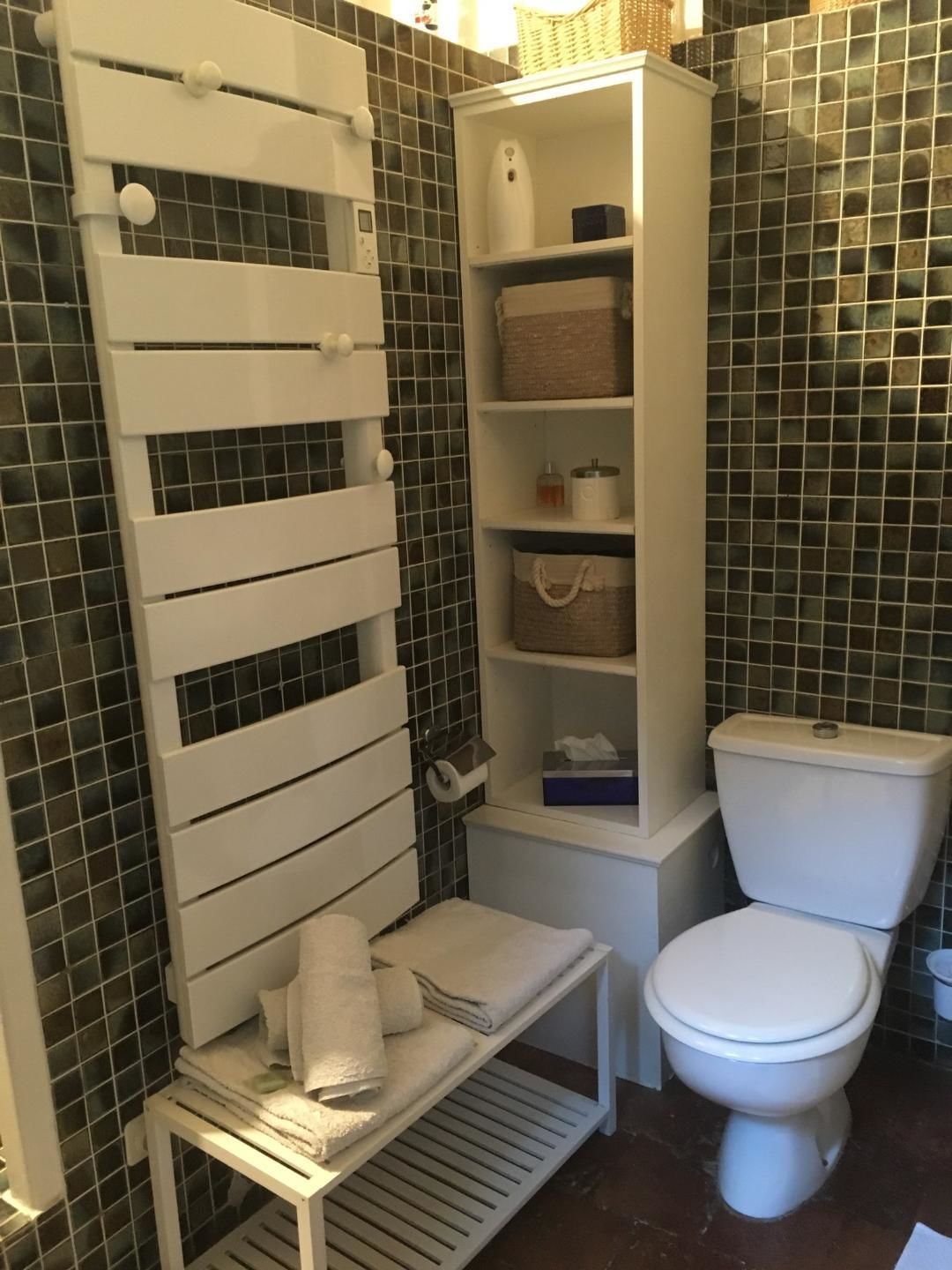 Ein Badezimmer mit weißem Handtuchhalter, einer kleinen Ablage für Toilettenartikel, einer Toilette und einer Bank mit Handtüchern.