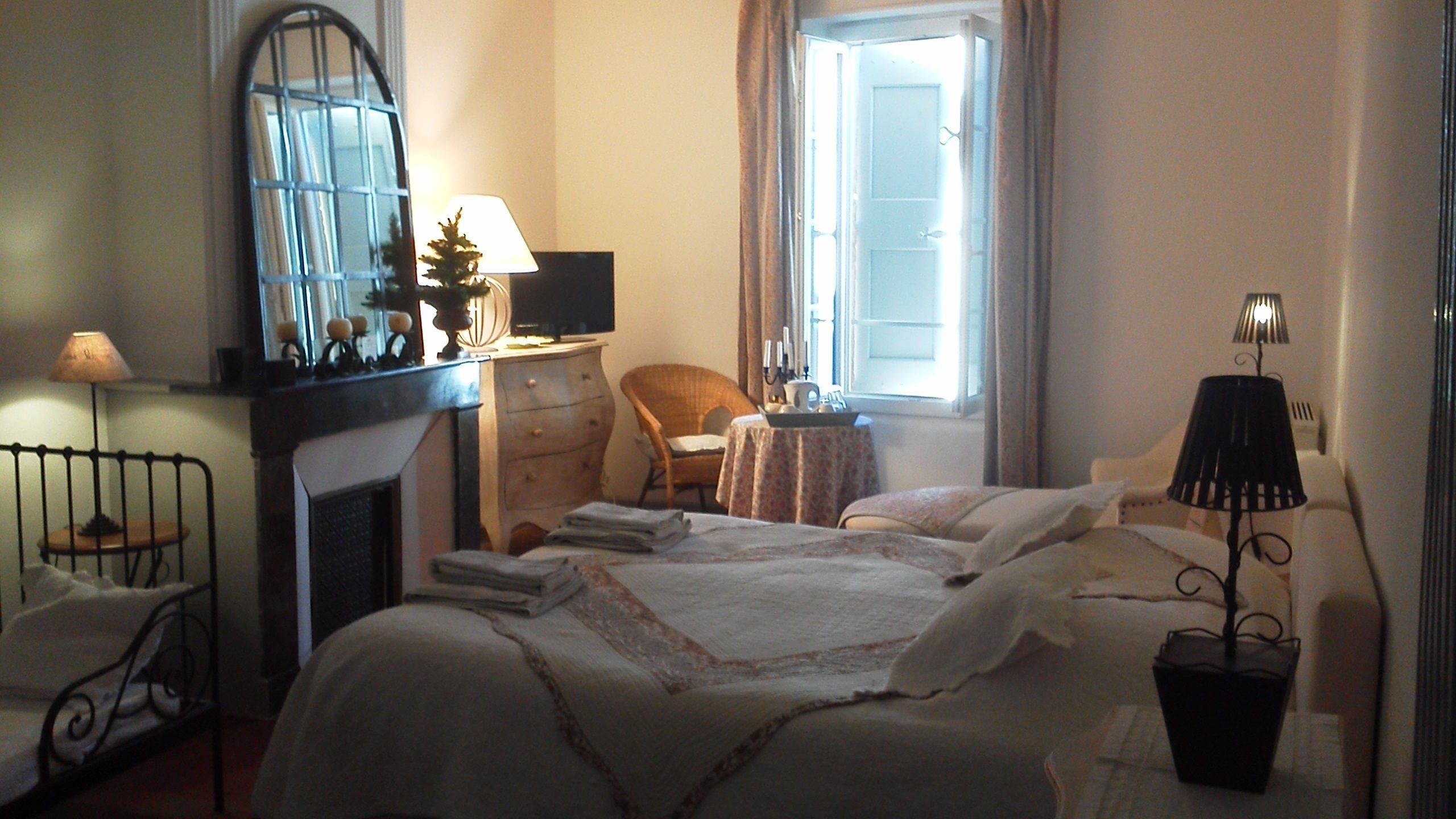 Un dormitorio con una cama, un tocador, una silla, una mesa, un espejo, una ventana y una lámpara.