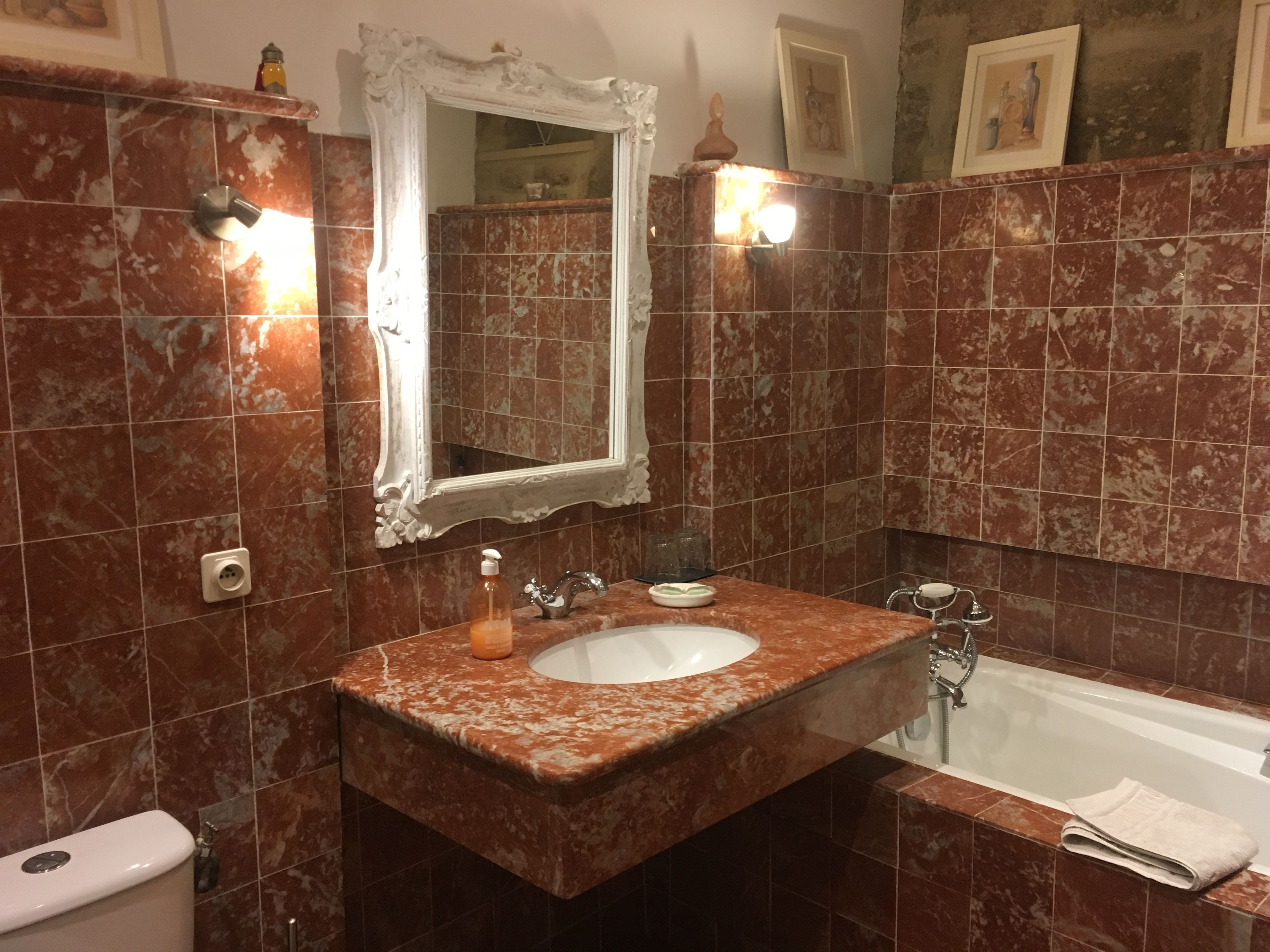 A bathroom with a marble sink, a white toilet, a bathtub, and a large mirror.