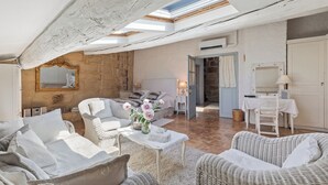 Un loft spacieux avec de hauts plafonds, des poutres apparentes, un mur en pierre et un coin salon confortable agrémenté de meubles en osier.