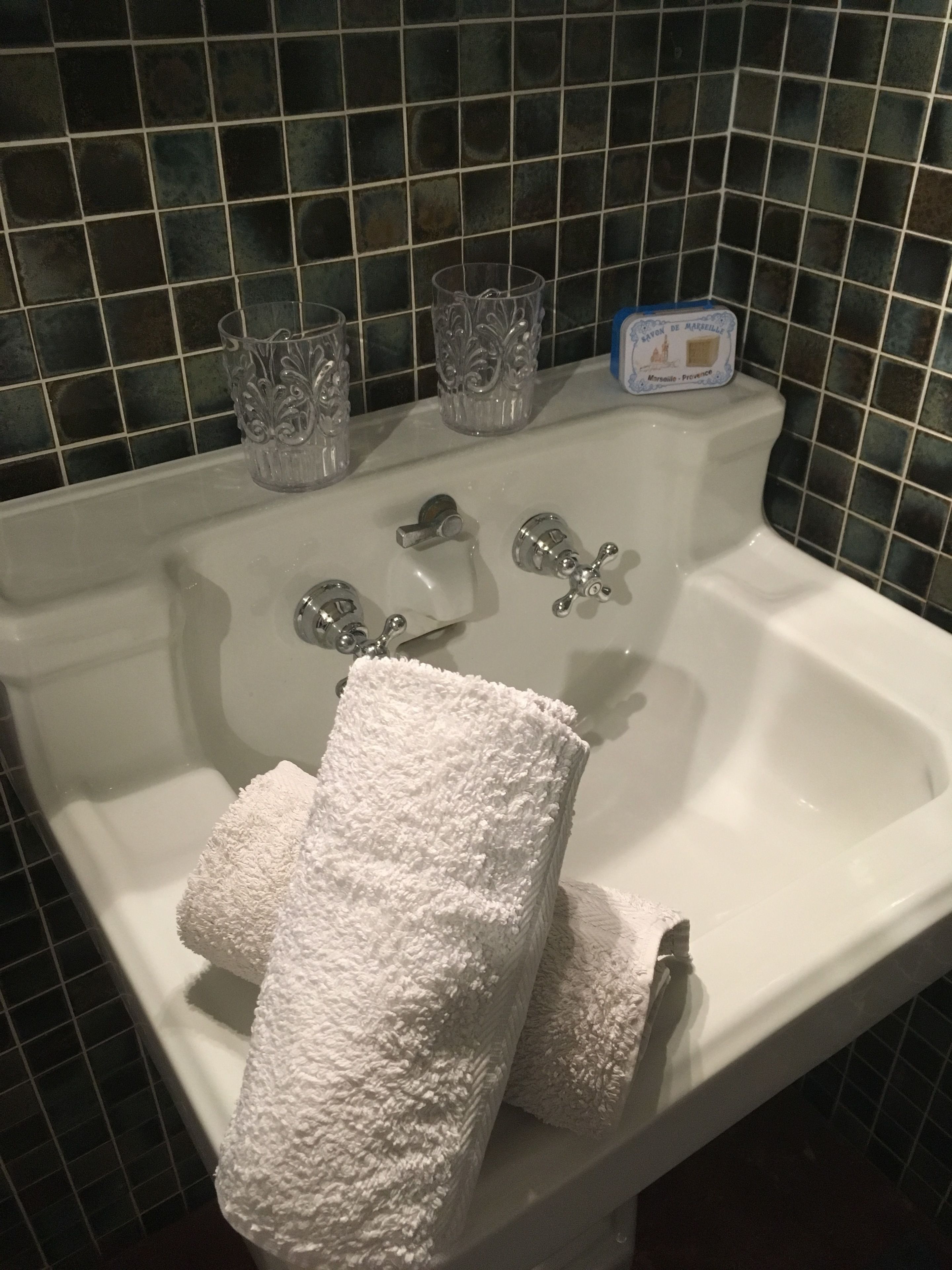 A bathroom sink with two glass vases, a soap dispenser, and two white towels.