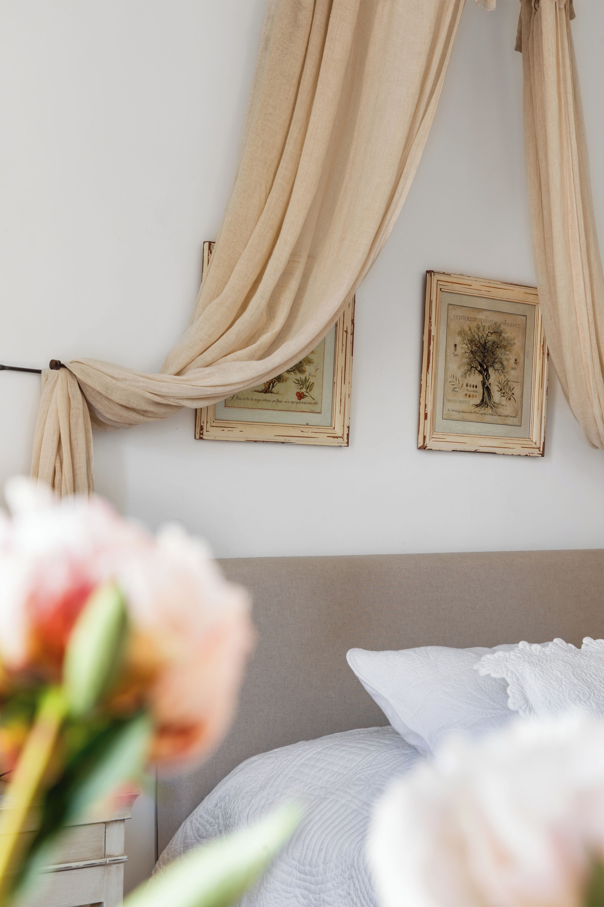 Une chambre à coucher avec un lit, des rideaux beiges et deux tableaux encadrés accrochés au mur.