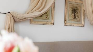 Une chambre à coucher avec un lit, des rideaux beiges et deux tableaux encadrés accrochés au mur.