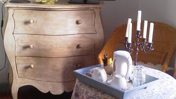 Une pièce comprenant une commode en bois, un téléviseur posé dessus, une table recouverte d’une nappe à motifs floraux et un chandelier avec des bougies.
