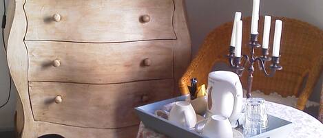 A room with a wooden dresser, a television on top, a table with a floral tablecloth, and a candelabra with candles.