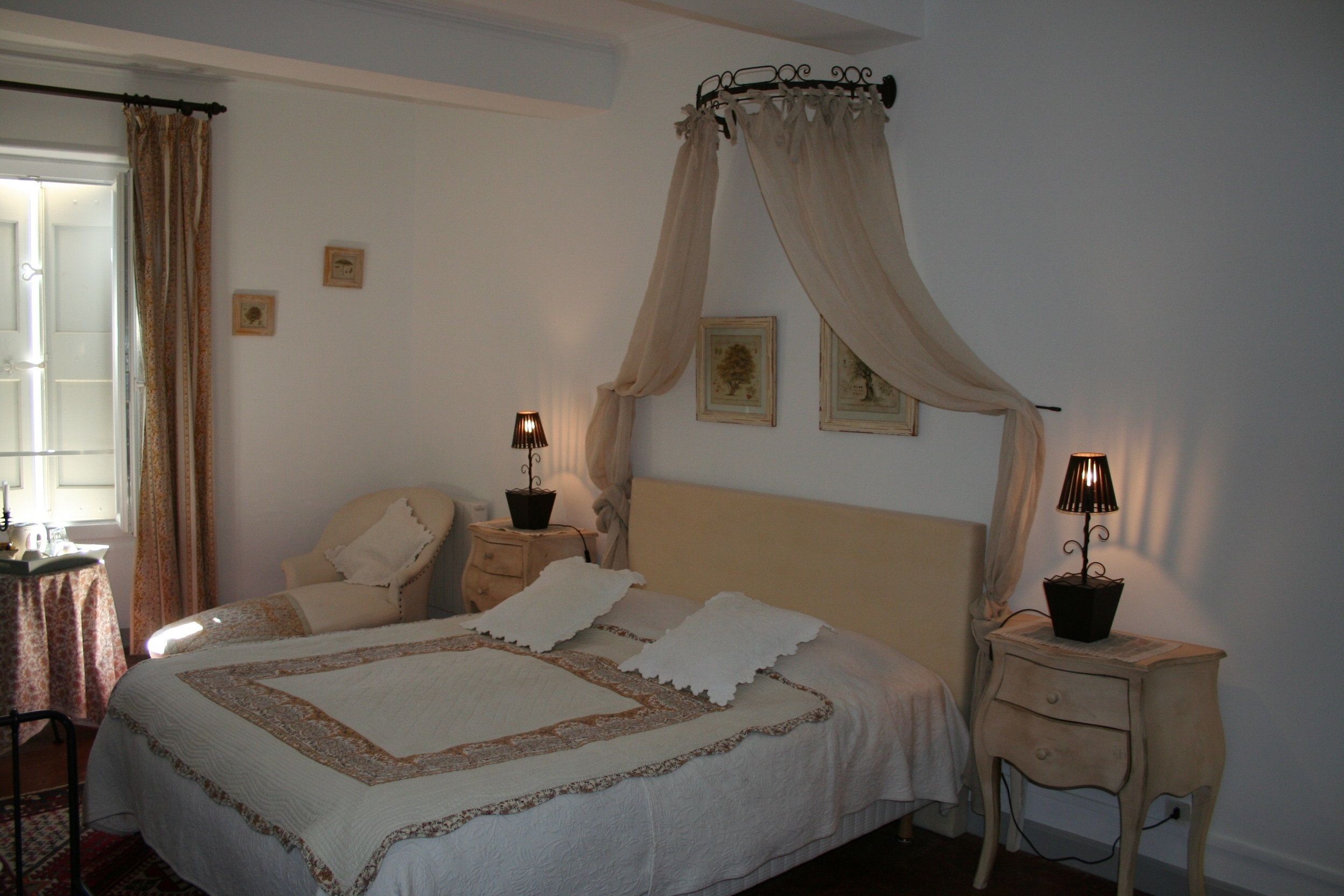 A bedroom with a large bed, two bedside tables with lamps, a chair, and a window with curtains.