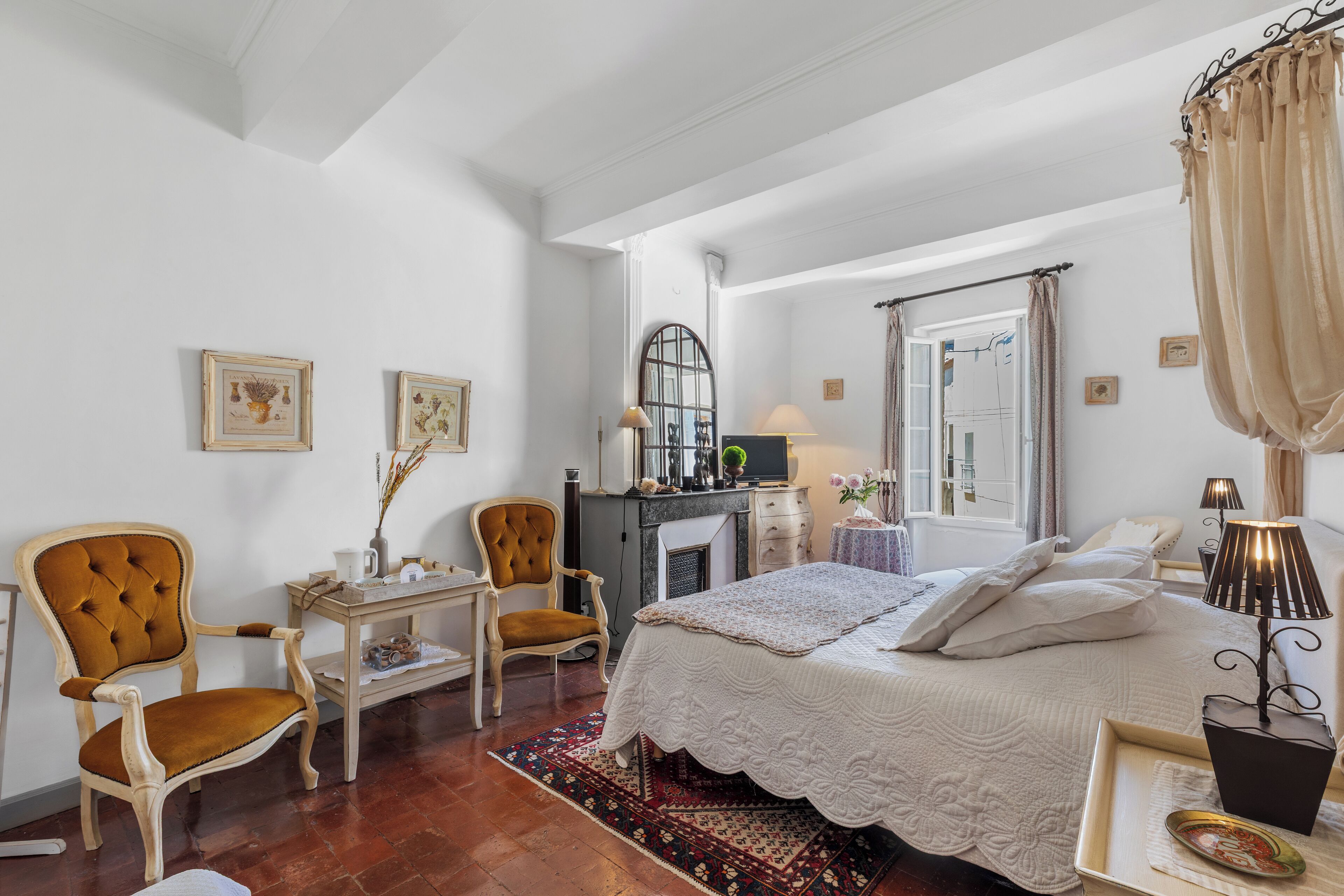 A bedroom with a bed, two chairs, a desk, a dresser, and a mirror.