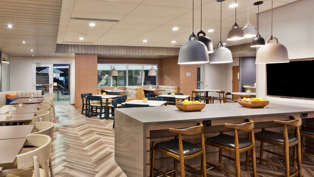 A modern restaurant with a central bar area, seating arrangements, and a herringbone patterned floor. - Fairfield Inn & Suites by Marriott Birmingham Colonnade (Birmingham)