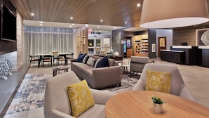 A modern hotel lobby with a reception desk, seating area, and a dining space. - Fairfield Inn & Suites by Marriott Birmingham Colonnade (Birmingham)