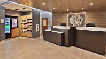 A modern reception area with a wooden reception desk, a refrigerator stocked with beverages, and shelves with snacks.
