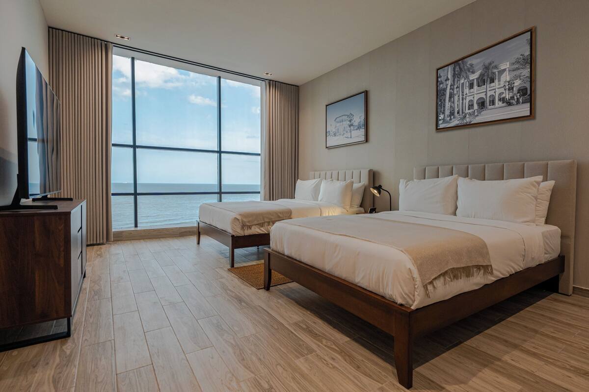 A hotel room with a large window, two beds, a TV, and a framed picture on the wall.