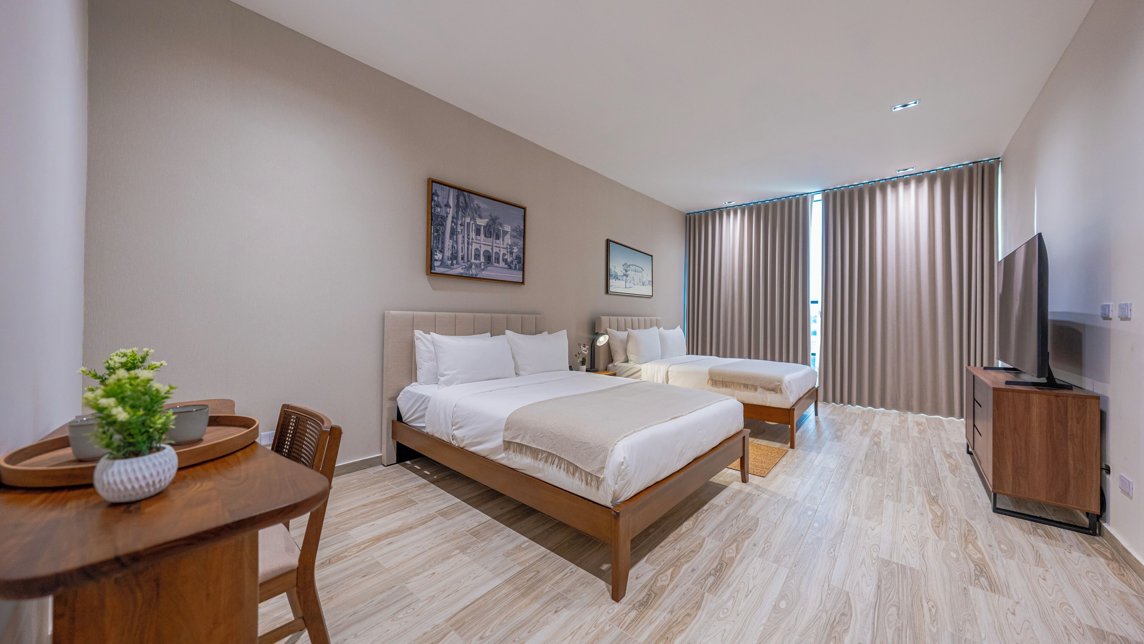 A hotel room with two beds, a desk, a TV, and a dining table.