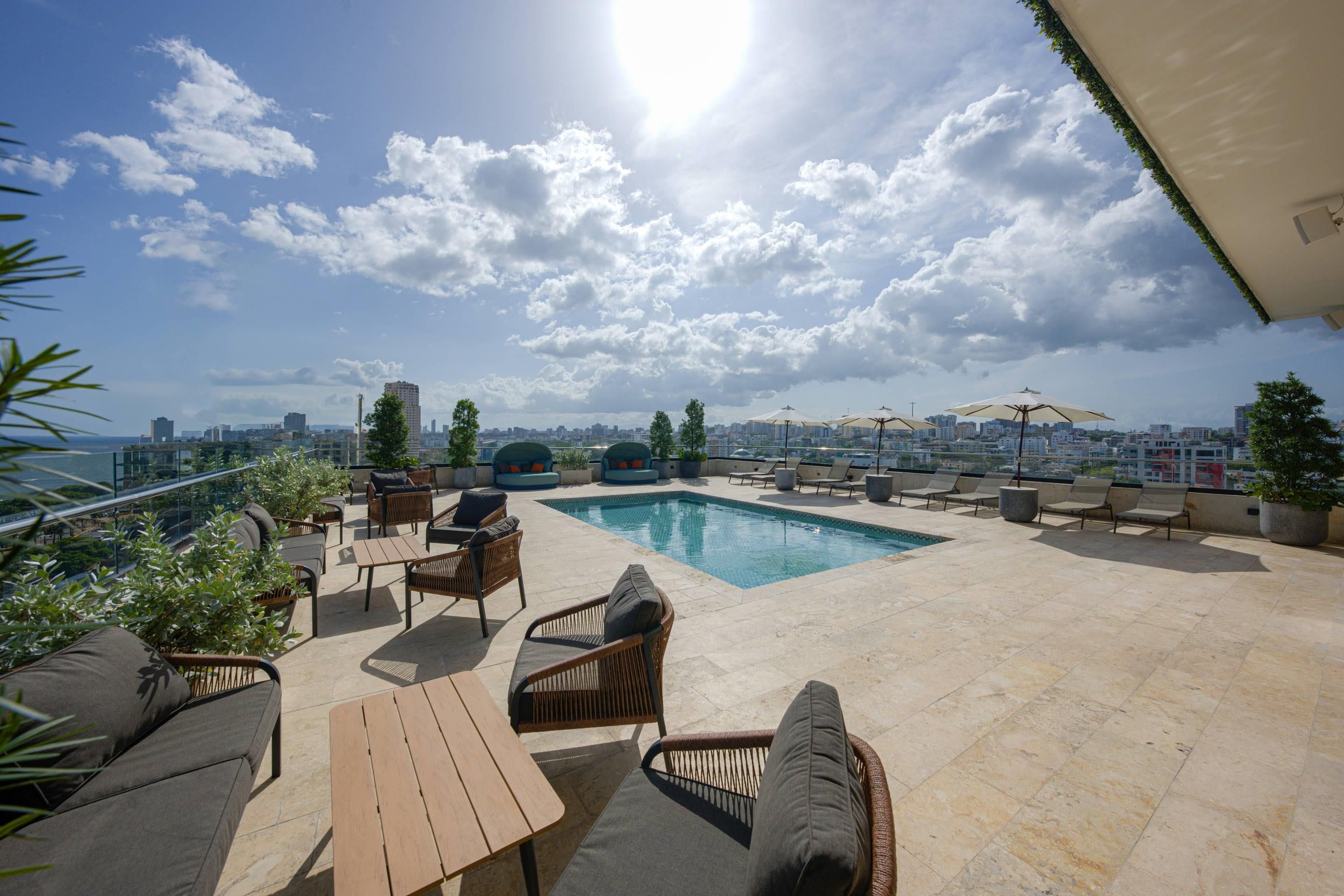 A rooftop pool area with lounge chairs, a pool, and a cityscape view.