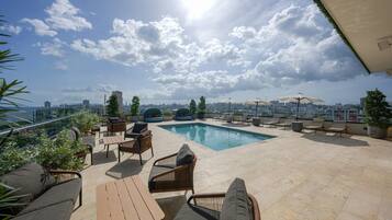 A rooftop pool area with lounge chairs, a pool, and a cityscape view.