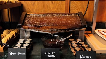 A buffet with labeled containers of peanut butter, Miel En Panal, and Nutella.