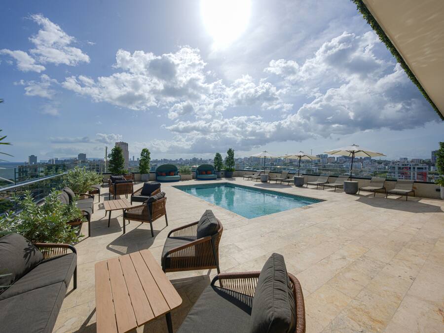 Uma área de piscina no terraço com espreguiçadeiras, uma mesa de madeira e vista para o horizonte da cidade.
