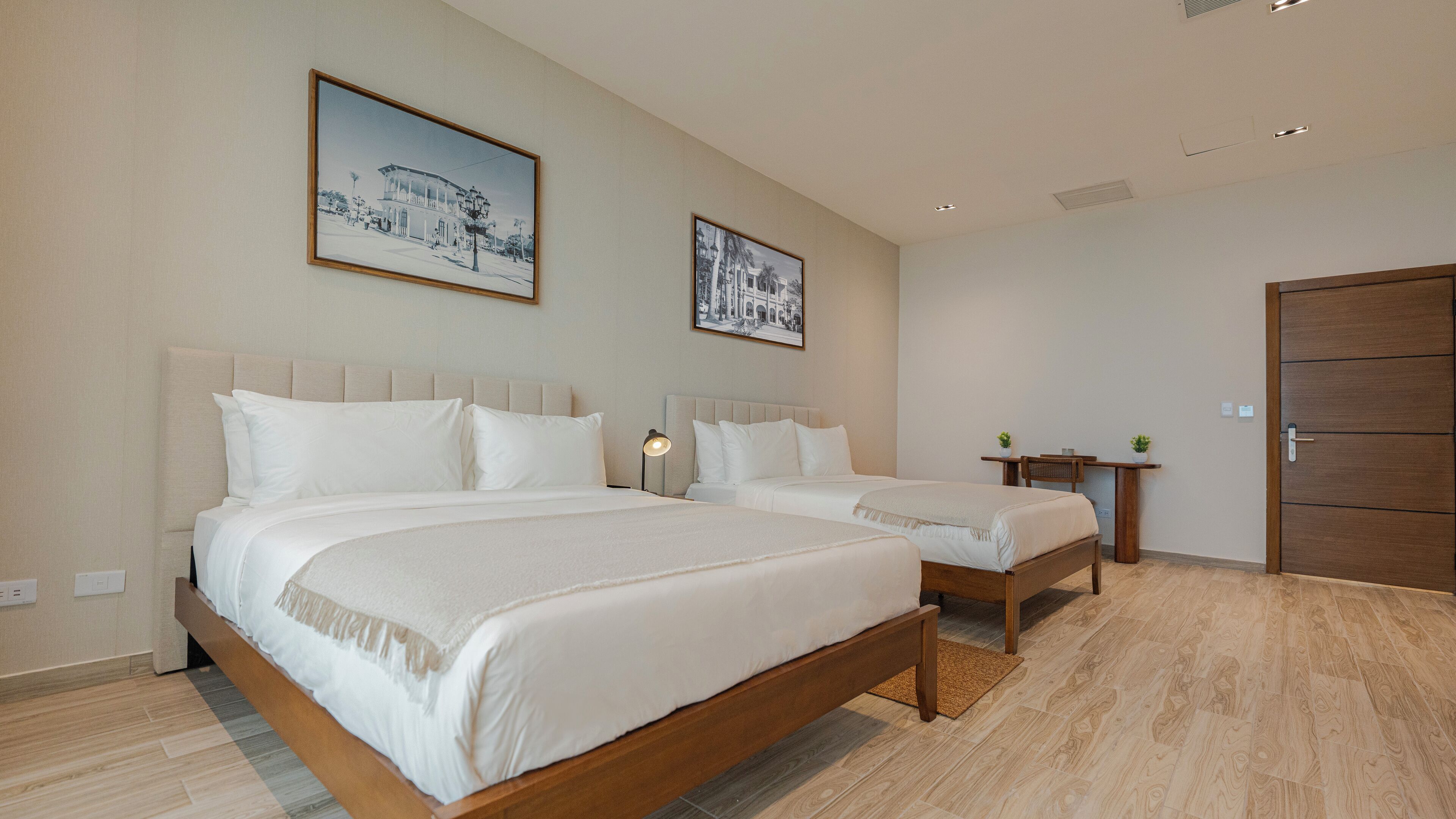 Een hotelkamer met twee bedden, een bureau en twee foto's in lijsten aan de muur.