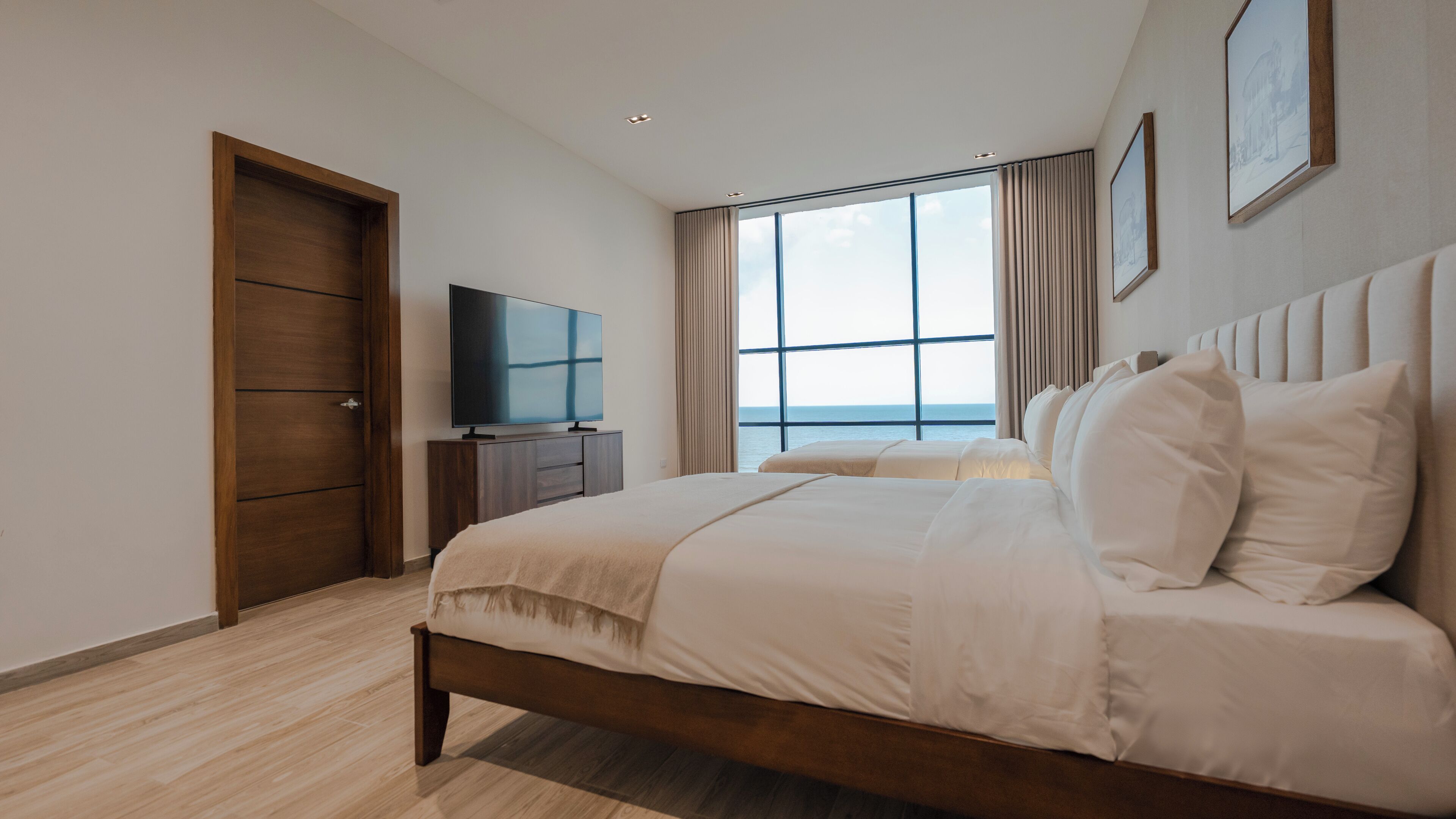 A modern bedroom with a large bed, a TV, and a view of the sea.