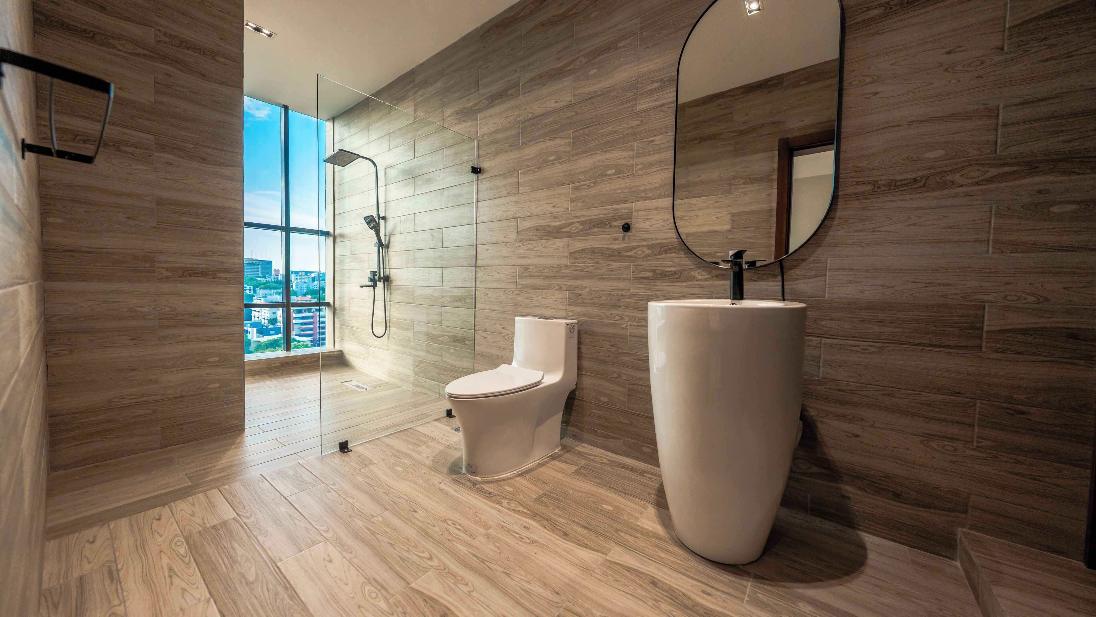 A modern bathroom with a large window, a shower, a toilet, and a large sink.