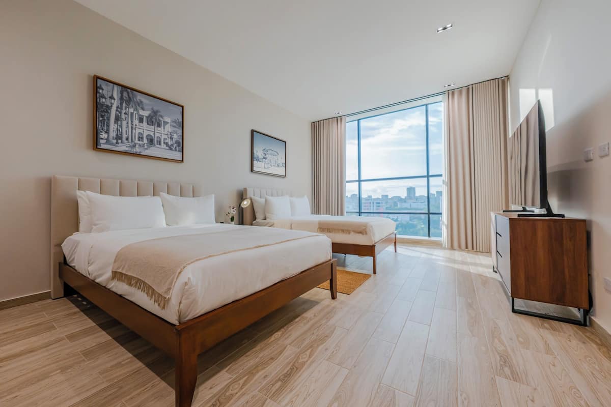 A modern hotel room with a large bed, a smaller bed, a TV, and a large window with a city view.