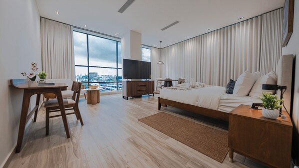 A modern hotel room with a large bed, a desk with a chair, a TV, and a view of the city through large windows. - Mauad Hotel Boutique & Spa, a member of Radisson Individuals (Santo Domingo)
