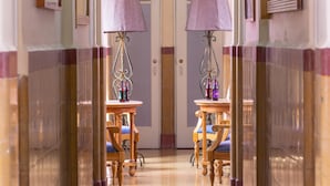 Un couloir d’hôtel avec des murs recouverts de miroirs, deux lampes et des chaises en bois dotées de coussins bleus.