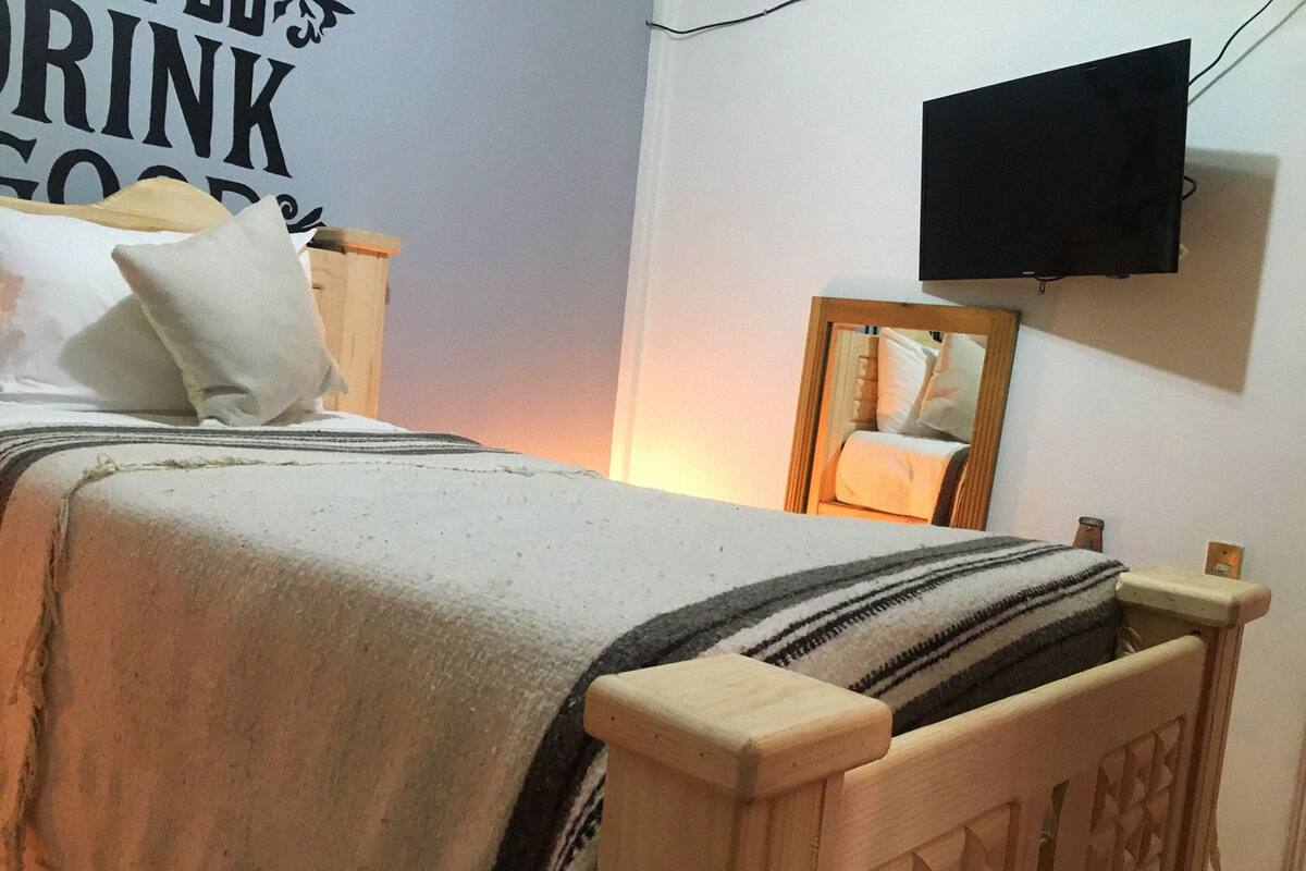 Une chambre à coucher avec un lit, une tête de lit en bois, un téléviseur fixé au mur et un miroir.
