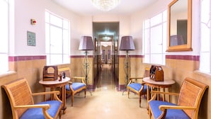Un hall d’hôtel agrémenté d’un lustre, de deux lampes, d’un miroir et de sièges avec des coussins bleus.