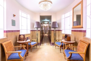 A hotel lobby with a chandelier, two lamps, a mirror, and seating with blue cushions.