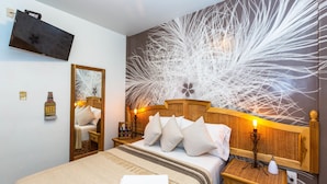 Une chambre d’hôtel avec un grand lit, une tête de lit en bois, un téléviseur fixé au mur, une table de chevet avec une lampe et un miroir.