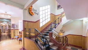 Un hall d’hôtel avec un escalier, un lustre et une enseigne indiquant « Bar sur le toit ».
