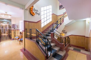 A hotel lobby with a staircase, a chandelier, and a sign that reads "Beer Roof".