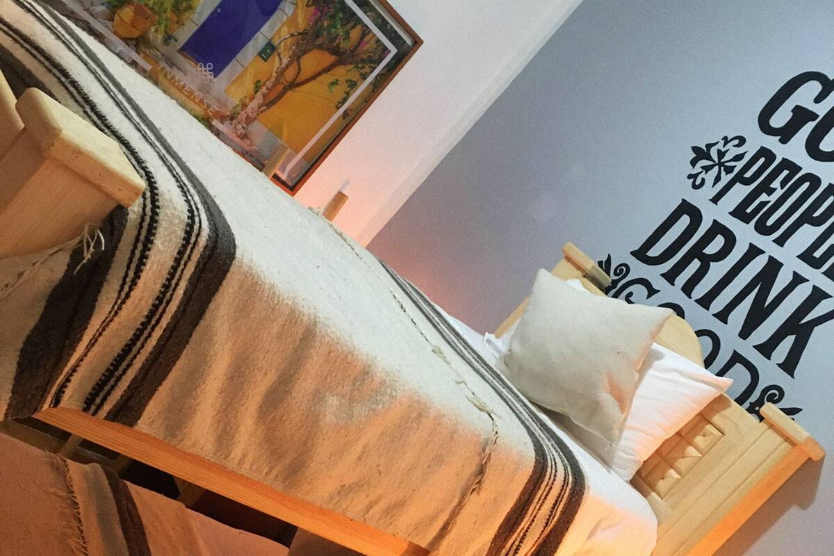 Un lit avec une couverture à rayures, un oreiller et une tête de lit en bois. Il y a un tableau au mur et une enseigne avec du texte.
