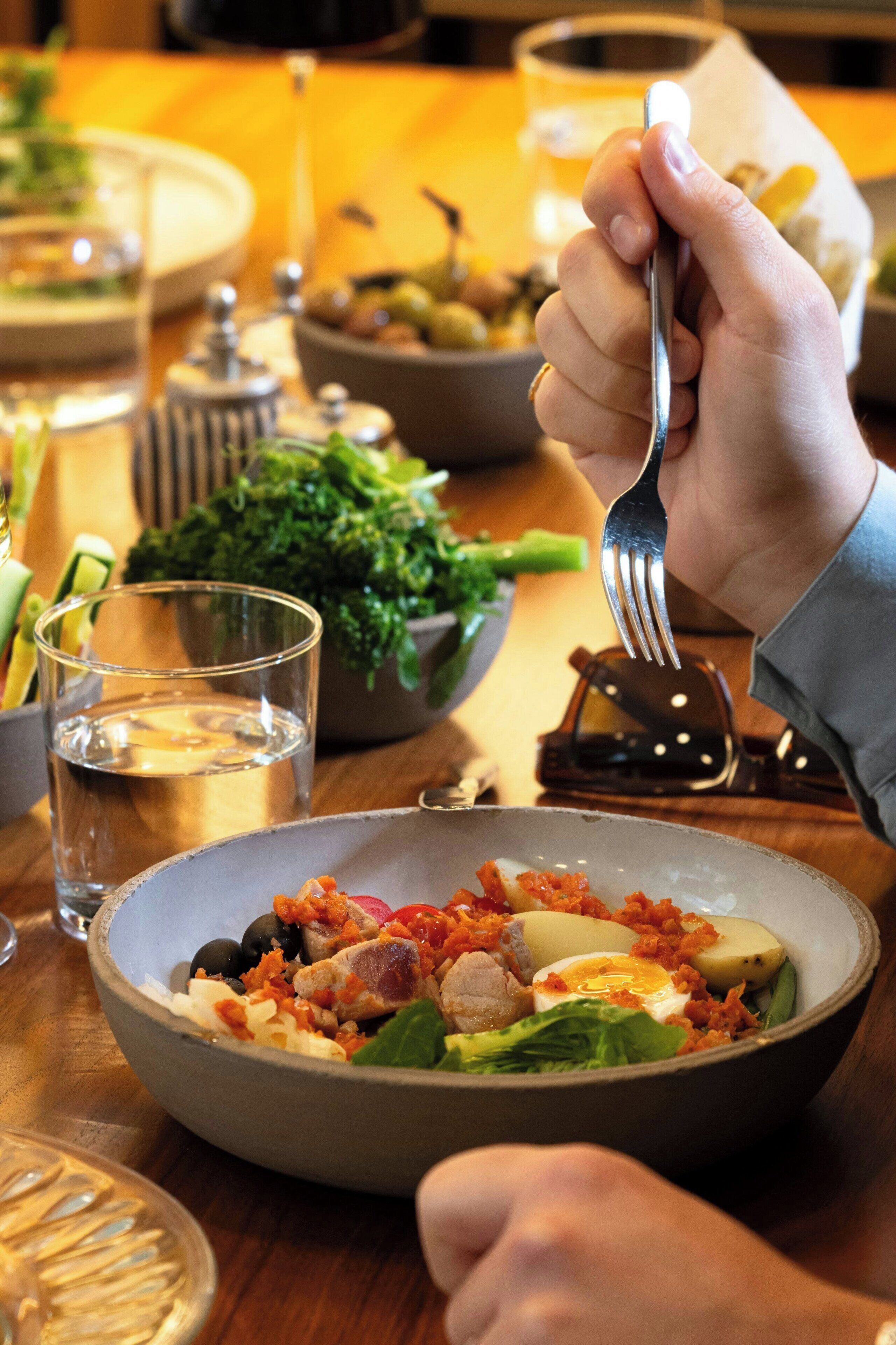 A dining table with a bowl of salad, a glass of water, and a fork.