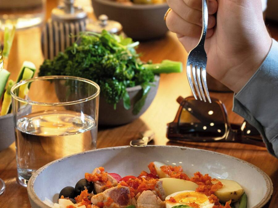 A dining table with a bowl of salad, a glass of water, and a fork.