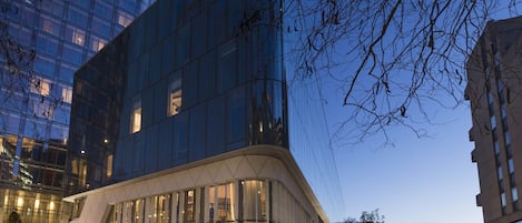 A modern hotel with a glass facade, a curved entrance, and a staircase leading to the lobby.