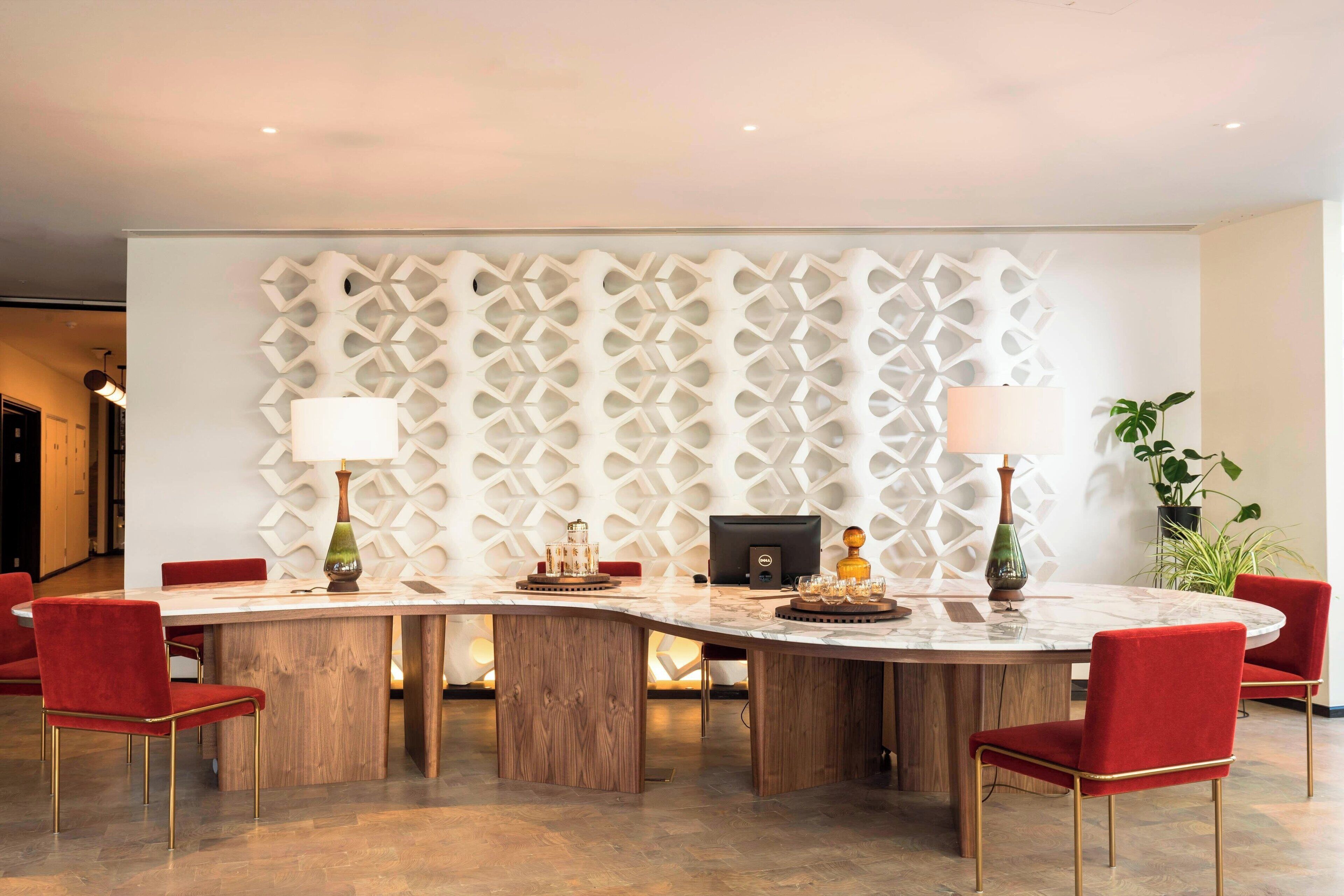 A modern dining area with a round table, red upholstered chairs, and a decorative wall panel.