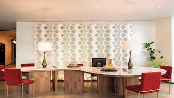 A modern dining area with a round table, red upholstered chairs, and a decorative wall panel.