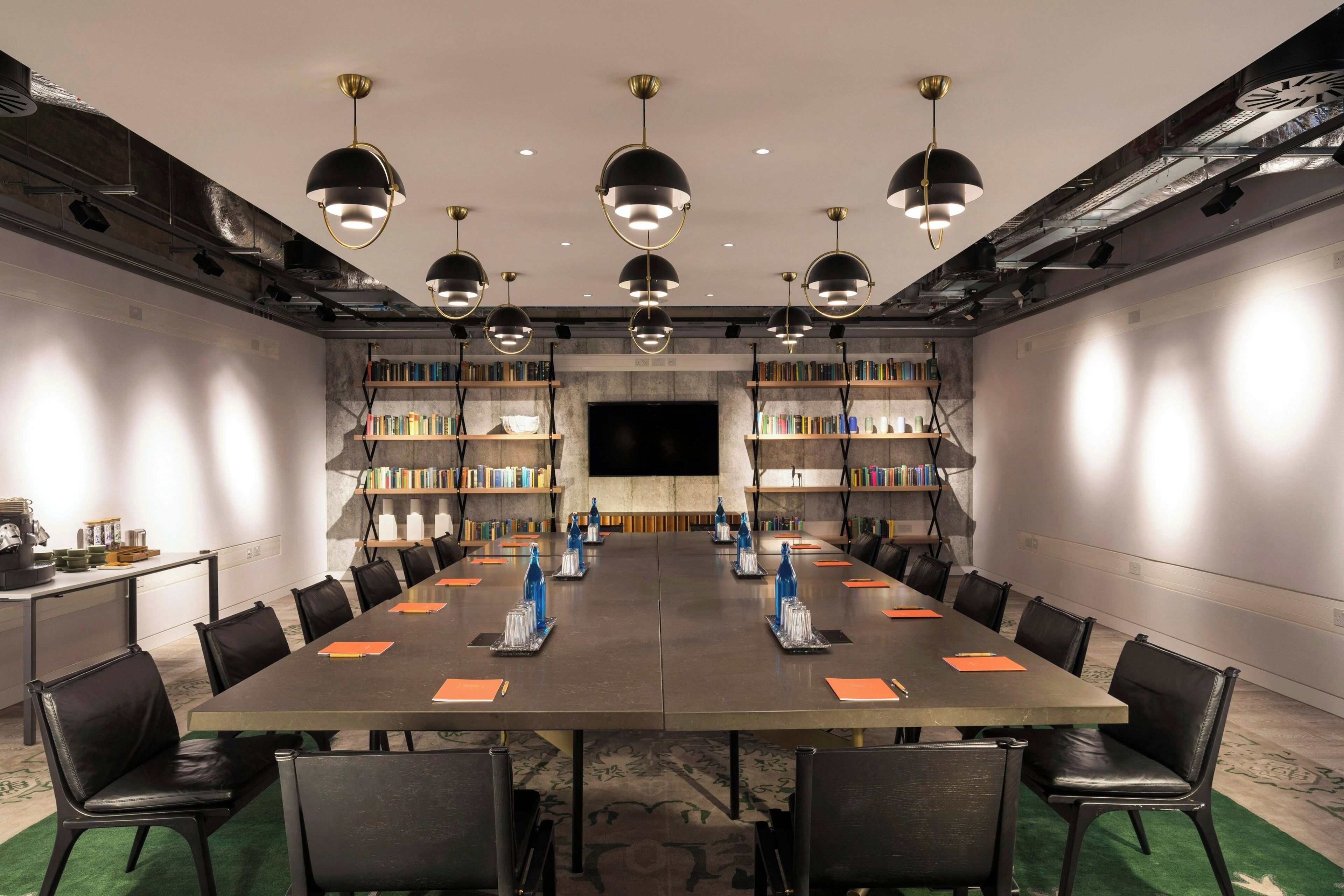 Ein Konferenzraum mit langem Tisch, Stühlen, Bücherregalen und Pendelleuchten.