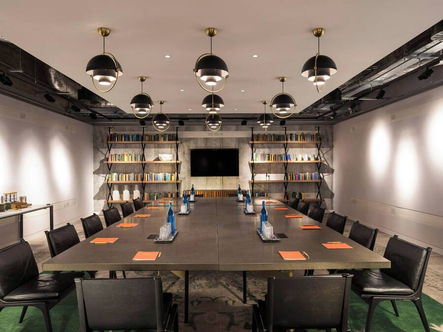 Ein Konferenzraum mit langem Tisch, Stühlen, Bücherregalen und Pendelleuchten.
