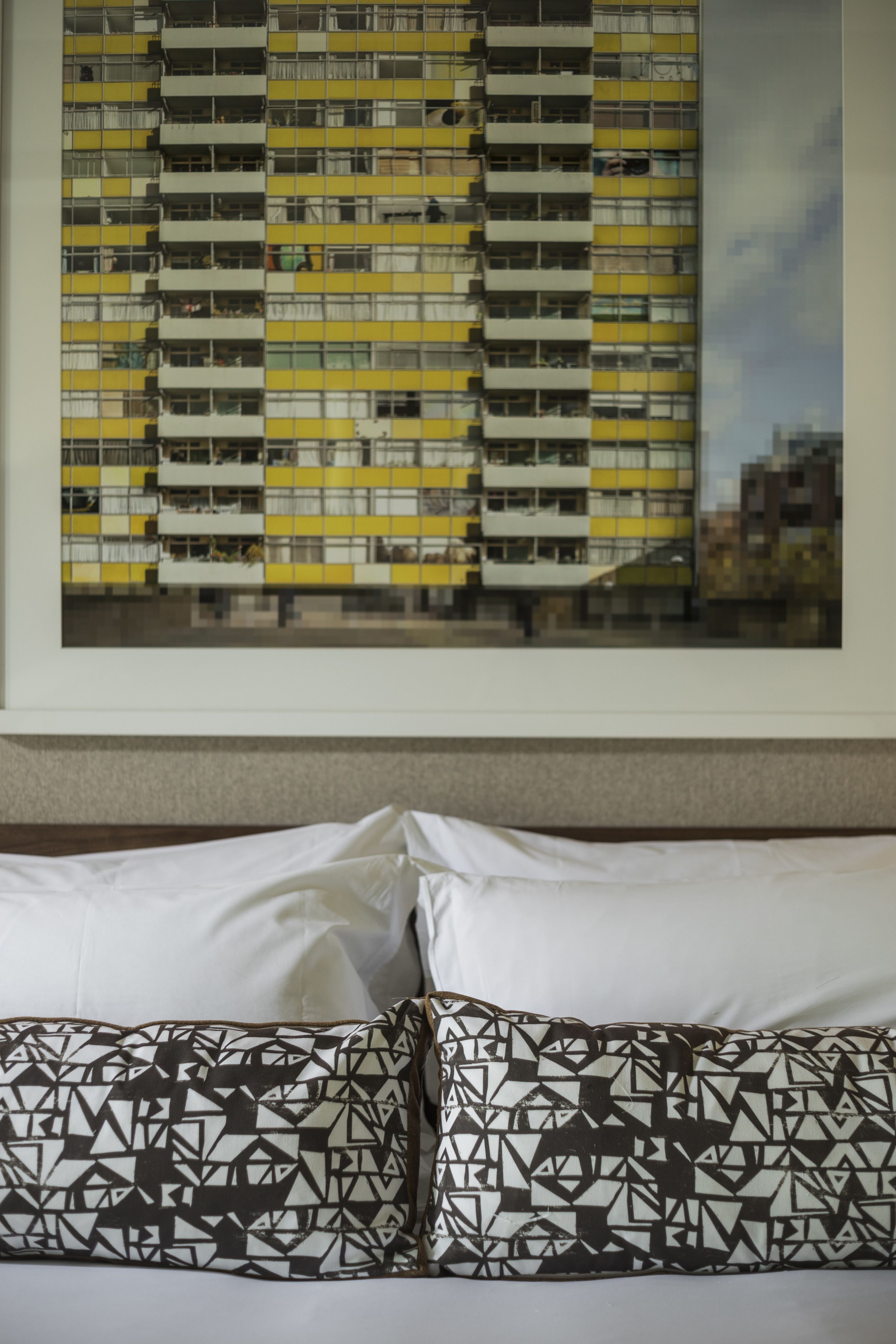 A hotel room with a bed, pillows, and a framed cityscape picture on the wall.